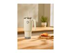 Cream-colored travel mug with a straw and handle on a wooden counter with oranges and ginger.