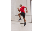 Man in CRIVIT sports shorts and red t-shirt exercising with ankle weights.