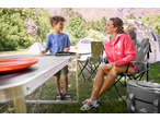 A woman and child camping, with a camping table, chairs, and tents in the background.