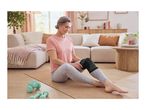 Woman wearing a knee support, sitting on a yoga mat with dumbbells nearby in a living room.