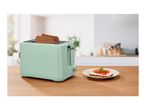 Mint green toaster with two slices of bread, next to a plate with toast and tomato.