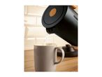 Black kettle with wooden accents pouring water into a light grey mug on a wooden countertop.