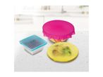 Three colorful silicone food covers in pink, blue, and yellow, covering bowls of food on a kitchen counter.