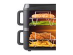 A black air fryer with two racks cooking food, including chicken and fries.