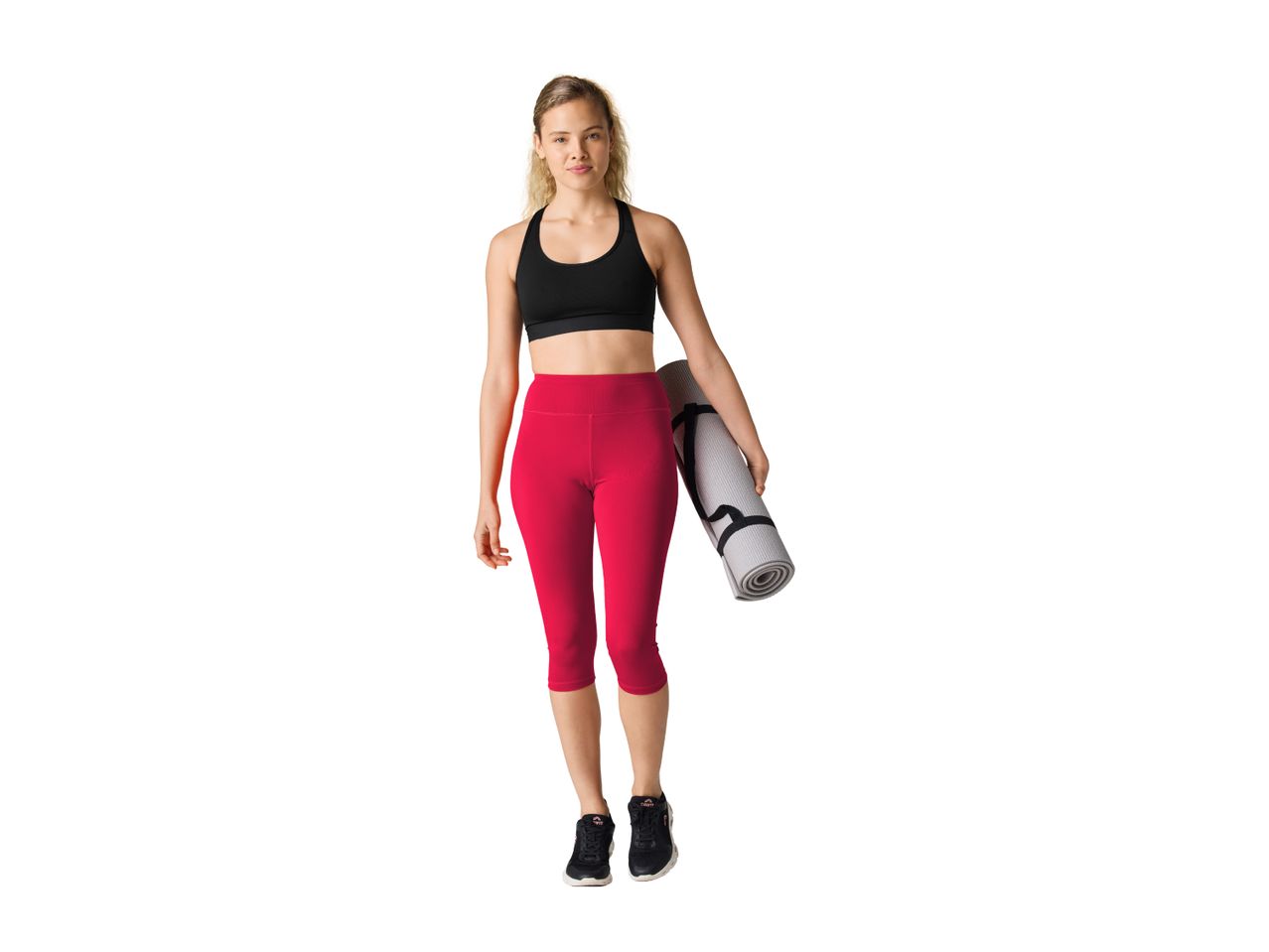 Woman in black sports bra and red capri leggings holding a yoga mat.