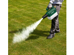 Persoană care folosește un suflant de frunze verde și alb pe gazon, cu un jet de fum.