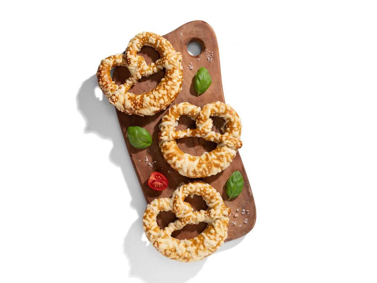 Három sajtos perec bazsalikommal és paradicsommal egy fa vágódeszkán.