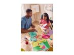 Father and daughter crafting with colorful paper, scissors, and glue on a wooden table.