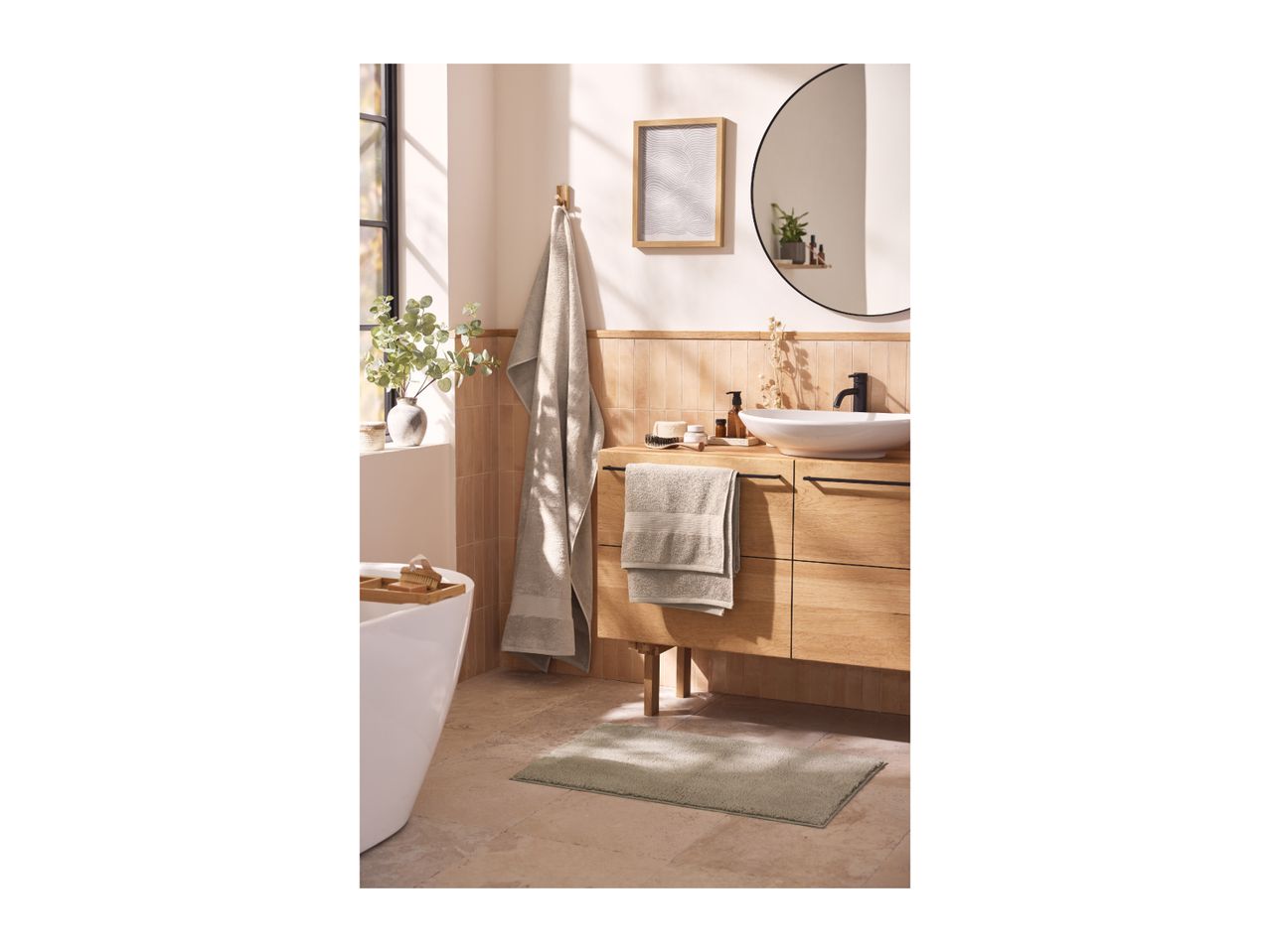 Bathroom with wooden vanity, white sink, round mirror, and light green bath mat.
