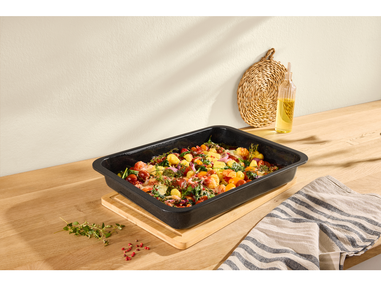 Baked gnocchi with vegetables and herbs in a black baking dish on a wooden counter.