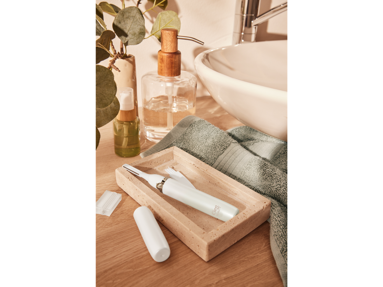 A white facial hair remover and accessories on a tray next to a sink with soap and a plant.