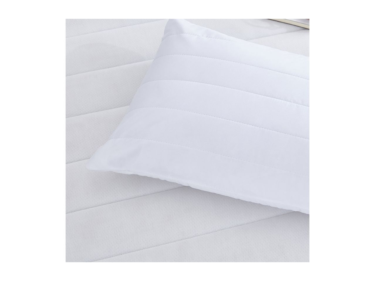 White quilted pillow on a white quilted mattress pad.