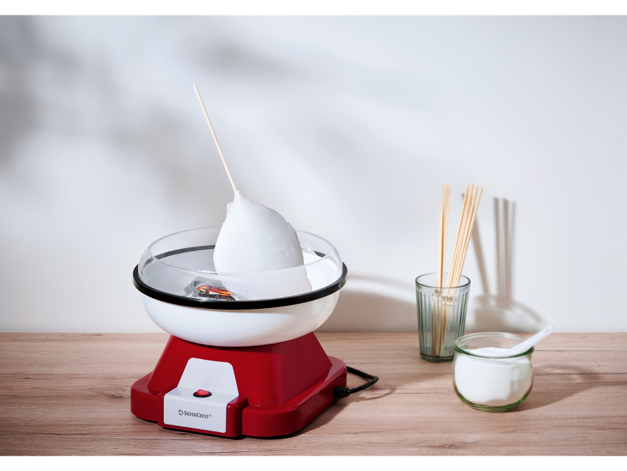 Silvercrest® mašina za šećernu vunu sa šećernom vunom, štapićima i šećerom na drvenom stolu.