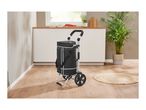 Black shopping trolley with white stripes in a modern kitchen with wooden floor and plants.