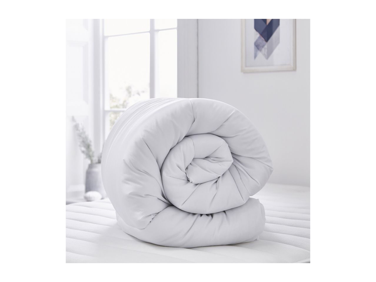 Rolled white duvet on a mattress in a bright room.