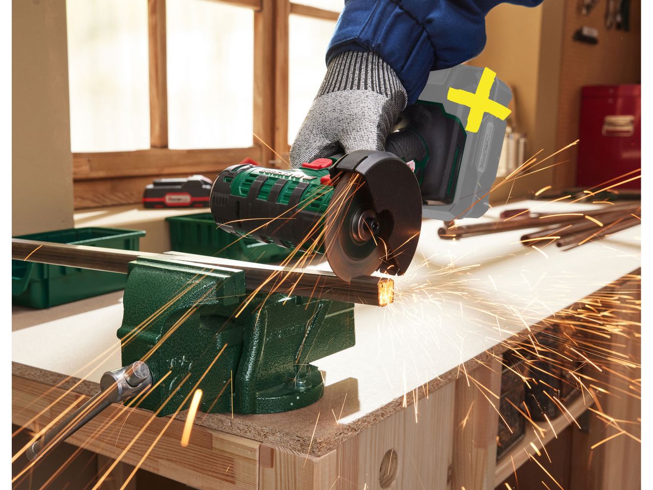 A person uses a PARKSIDE® Cordless Angle Grinder to cut metal in a workshop.