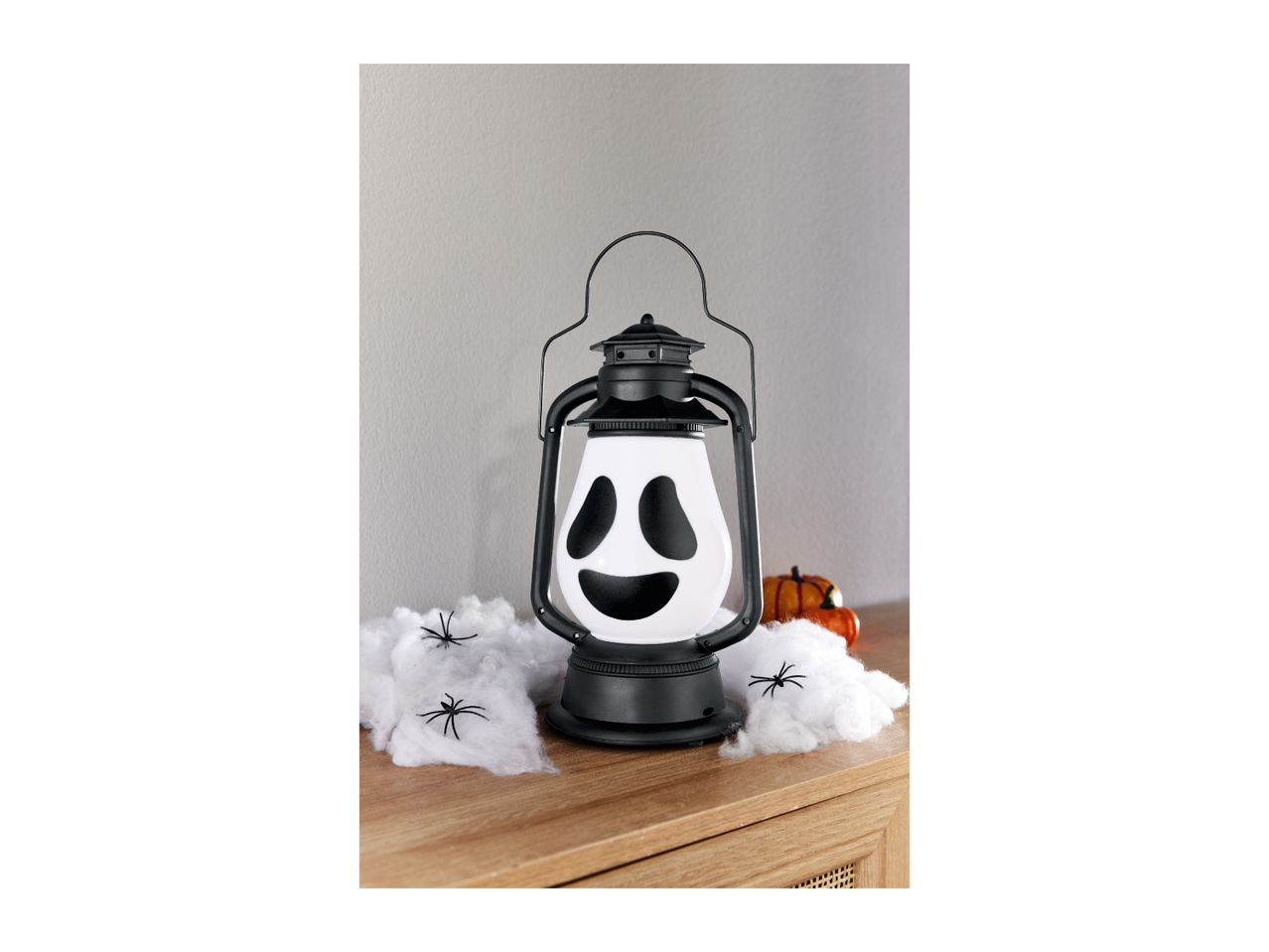 Halloween lantern with a ghost face, surrounded by fake spiderwebs and plastic spiders.