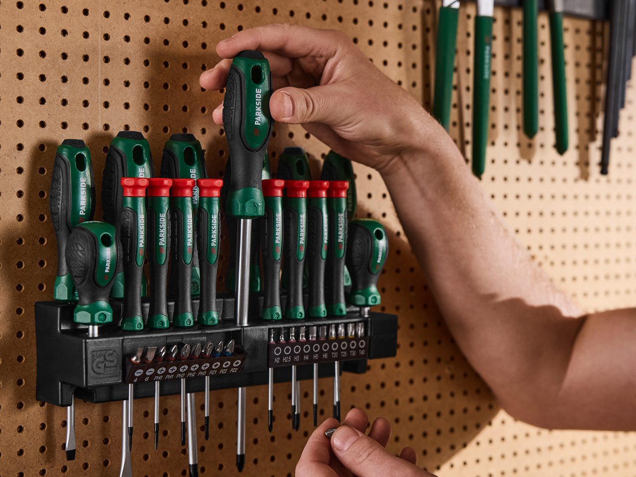 Το χέρι ενός ατόμου επιλέγει ένα κατσαβίδι από ένα σετ κατσαβιδιών και μύτες σε έναν διάτρητο πίνακα.