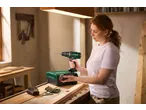 Woman holding a PARKSIDE® 20V Cordless Drill Driver, with a tool case and bits on a workbench.