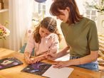 Una donna e una bambina disegnano su libri da grattare con un unicorno e un pavone.