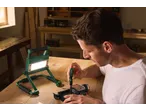 Homem repara câmara com chave de fendas e luz de trabalho numa mesa de madeira.