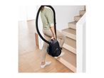 Person carrying a black vacuum cleaner up wooden stairs.