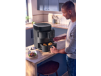 Man using a black air fryer with two baskets, cooking chicken and vegetables.