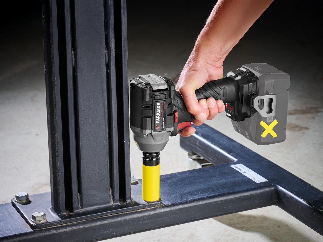 Férfi kéz tart egy akkus ütvecsavarozót, amely egy sárga dugókulccsal egy csavart rögzít.