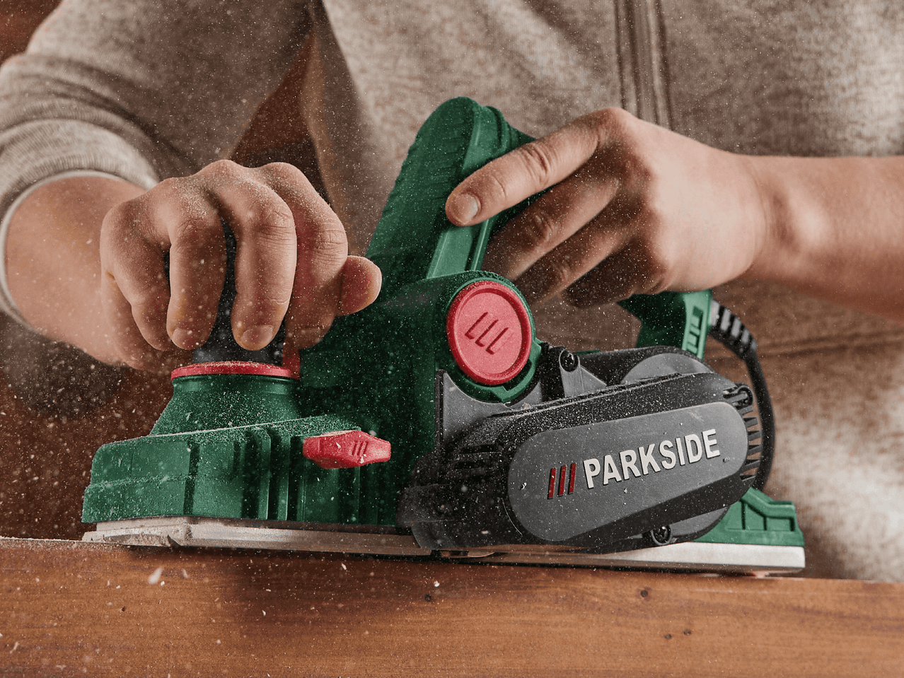 Ein Mann bearbeitet mit einer Parkside-Hobelmaschine ein Stück Holz.