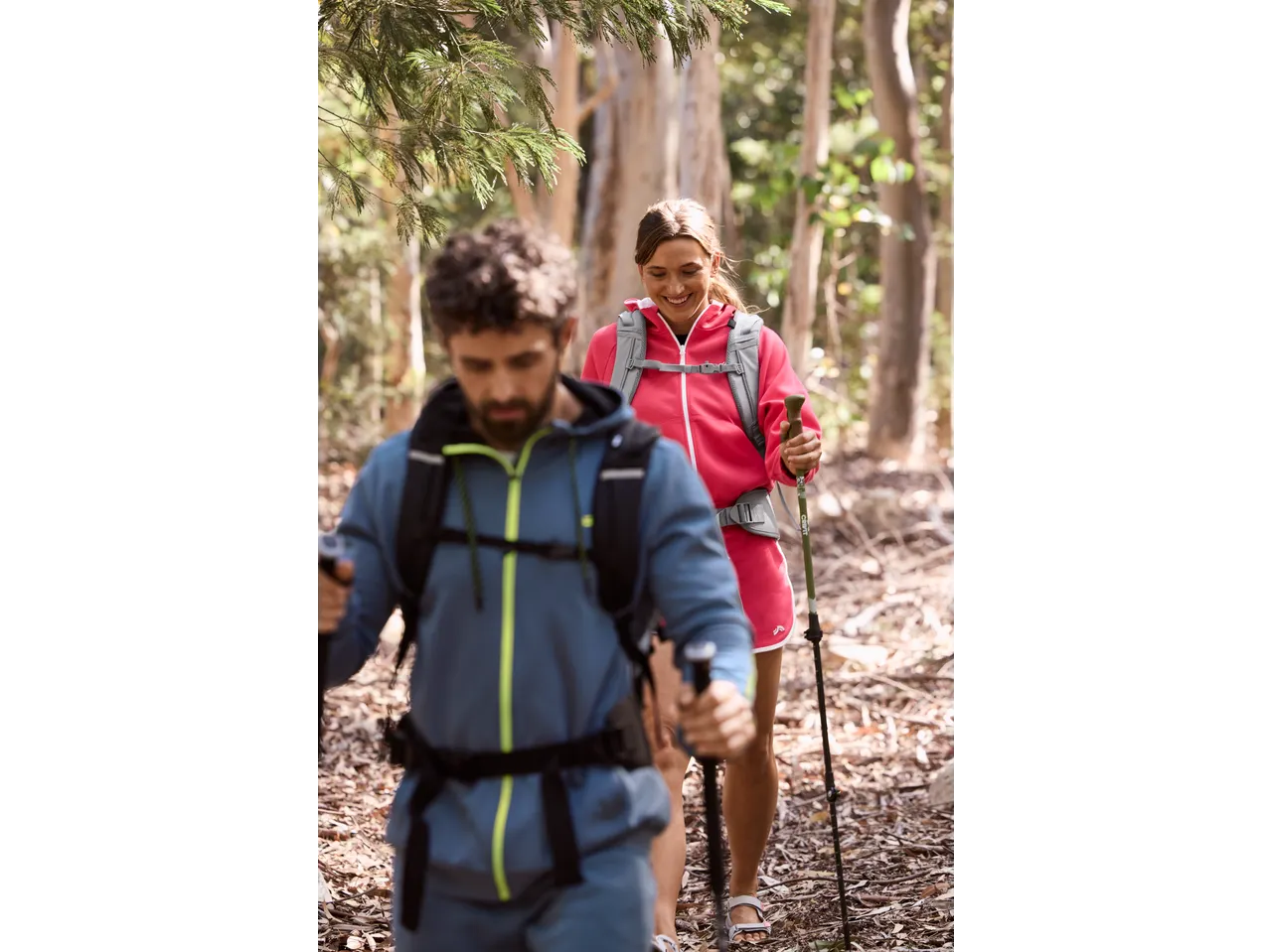 Two hikers with CRIVIT hiking backpacks and poles on a trail.