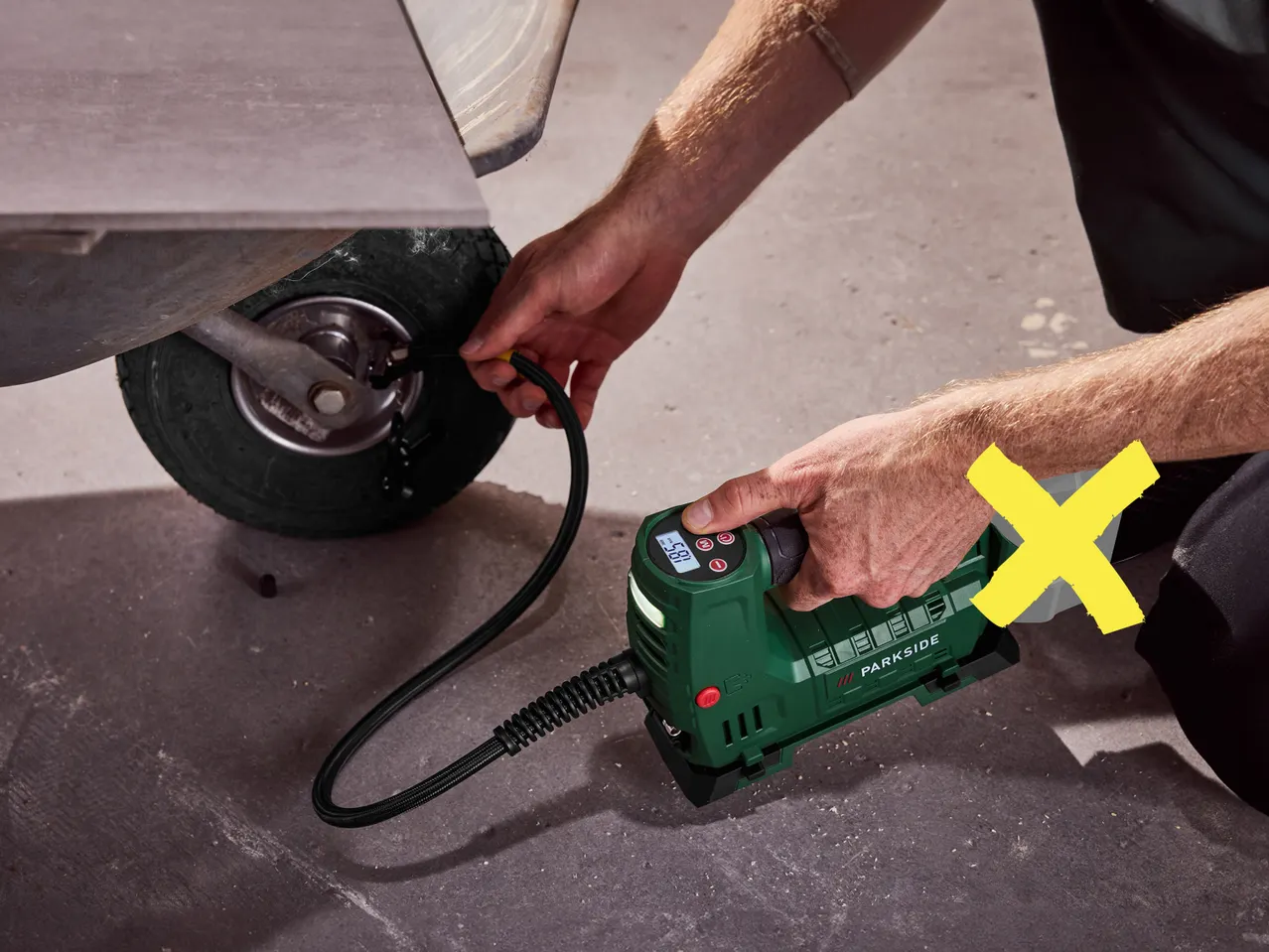 Un uomo gonfia la ruota di un carrello con un compressore portatile PARKSIDE.