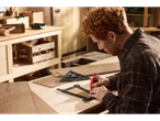 Man measuring and marking a wooden board using a square and a template.