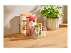 Clear organizer with couscous, rice, and spices on a wooden counter next to a basil plant.