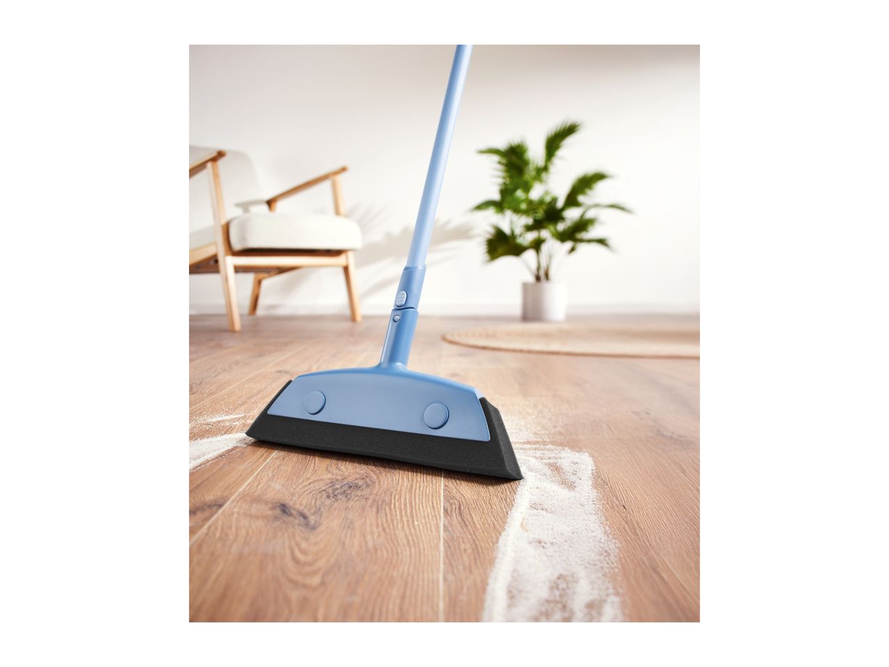 Blue broom sweeping white powder on a wooden floor in a living room.