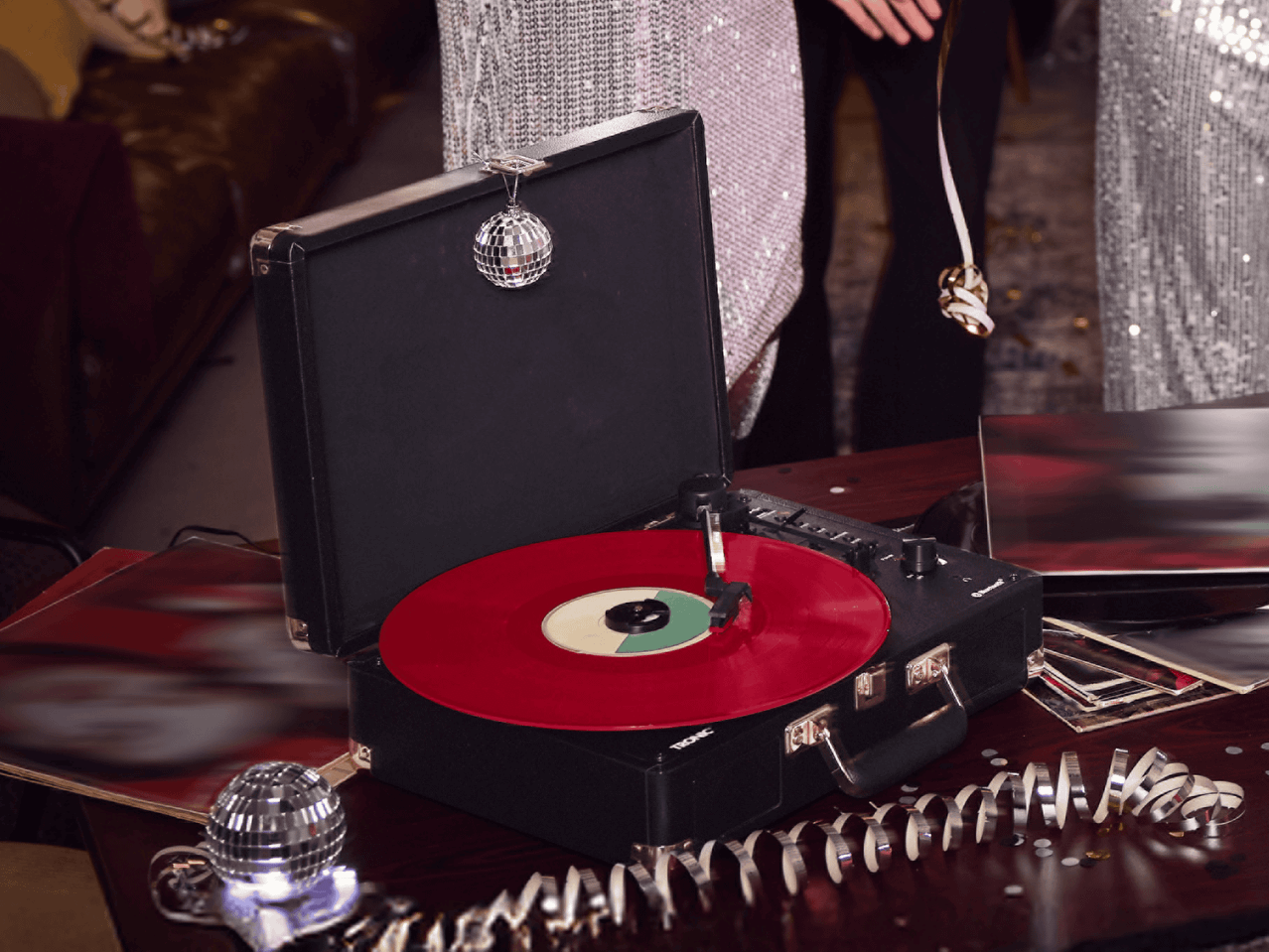 Schwarzer Plattenspieler mit roter Schallplatte und Disco-Dekoration auf einem Tisch.