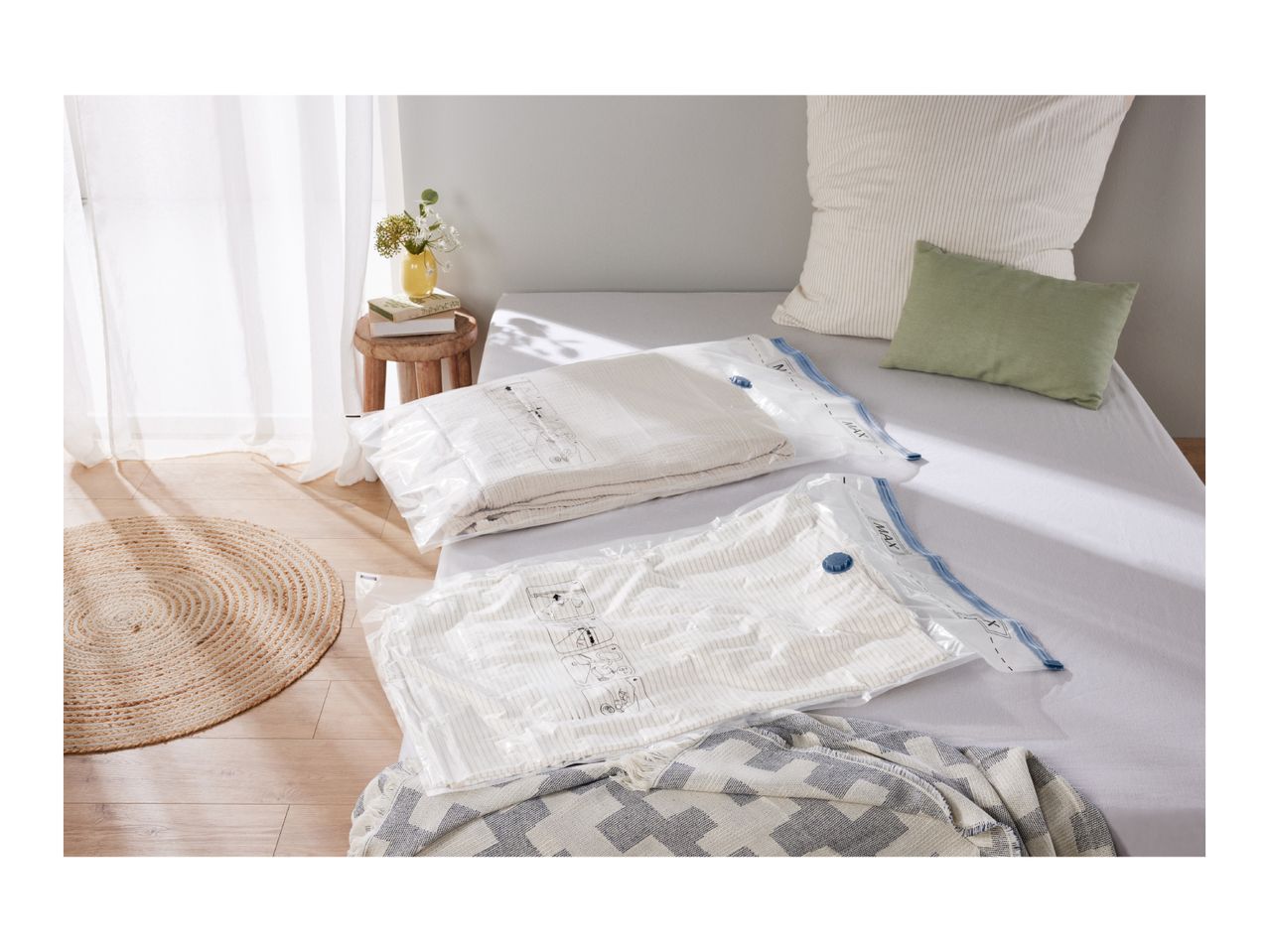 Two vacuum storage bags with textiles on a bed, with a rug and side table nearby.