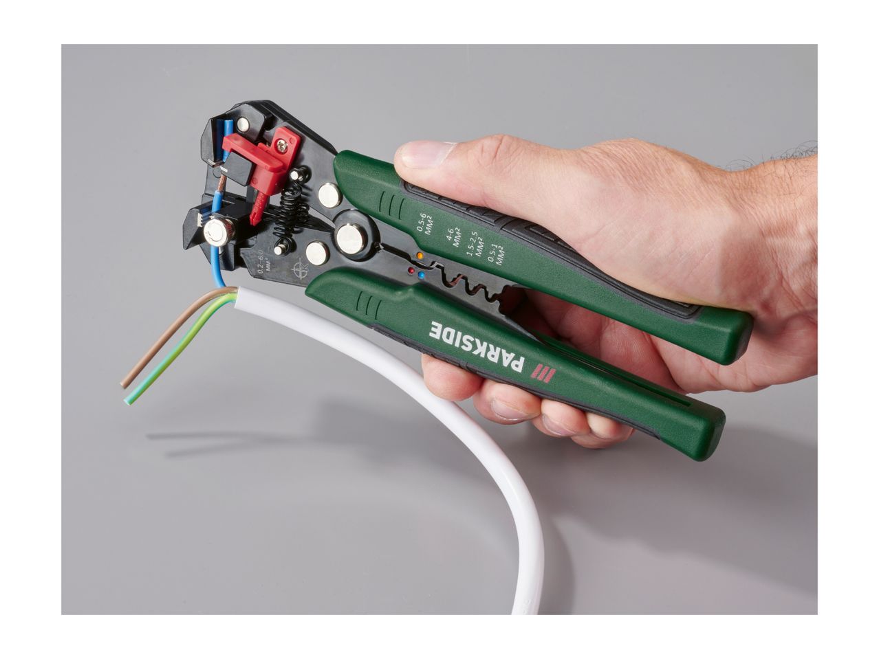 A hand holding Parkside wire strippers, stripping a blue wire from a white cable.