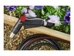 A black garden hose nozzle with a red trigger rests on a stone edge next to purple and white pansies.