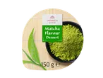 Matcha flavour dessert powder in a black bowl, with green tea leaves on a bamboo mat.