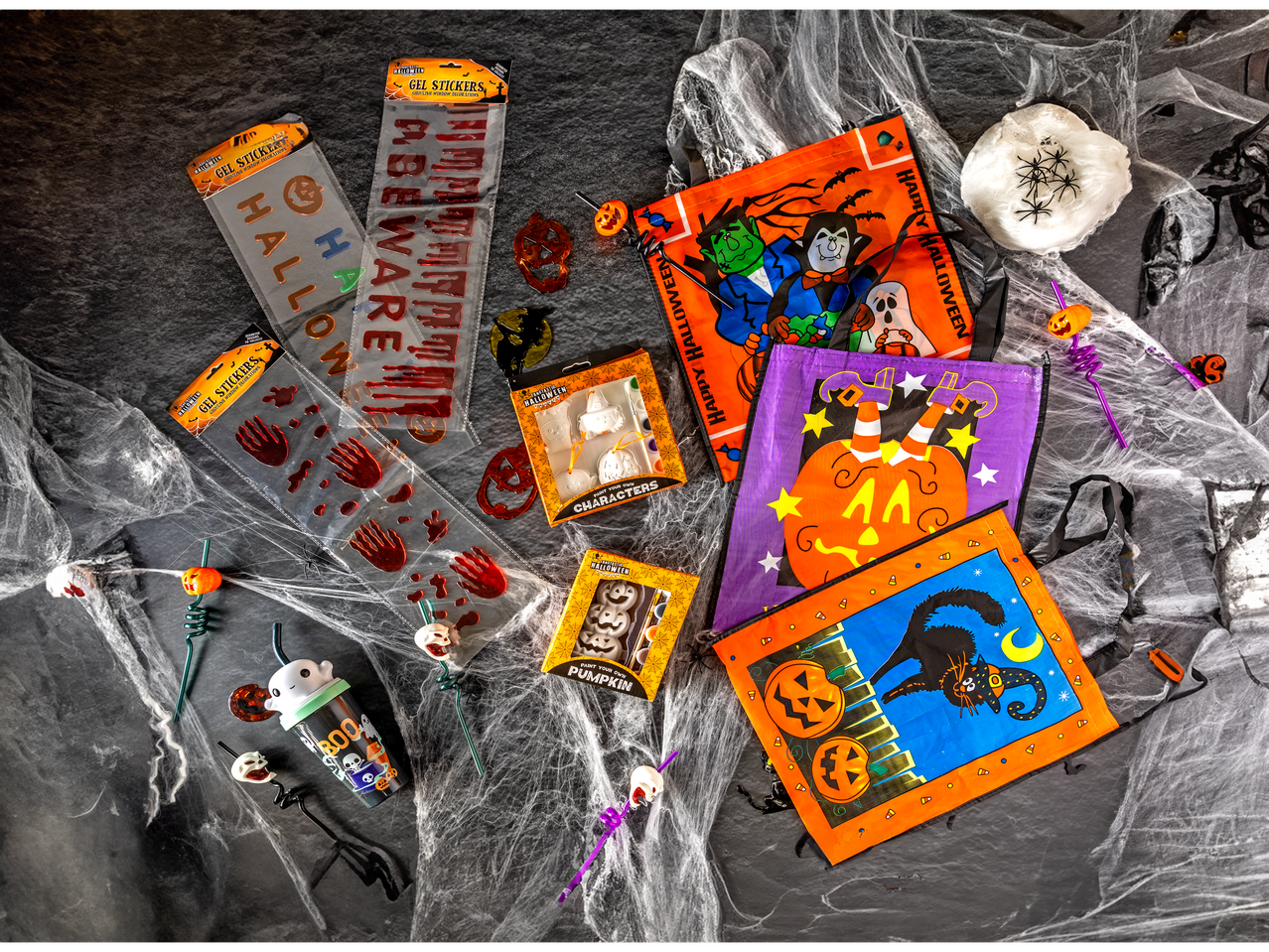 Halloween decorations including gel stickers, paint-your-own kits, and treat bags on a web-covered surface.