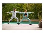 Man and woman in tracksuits doing yoga on mats outdoors.