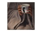 Hands holding a white mug with blue raindrop patterns, wrapped in a cozy blanket.