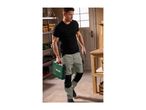 Man in work trousers carrying a toolbox and a utility knife in a workshop.