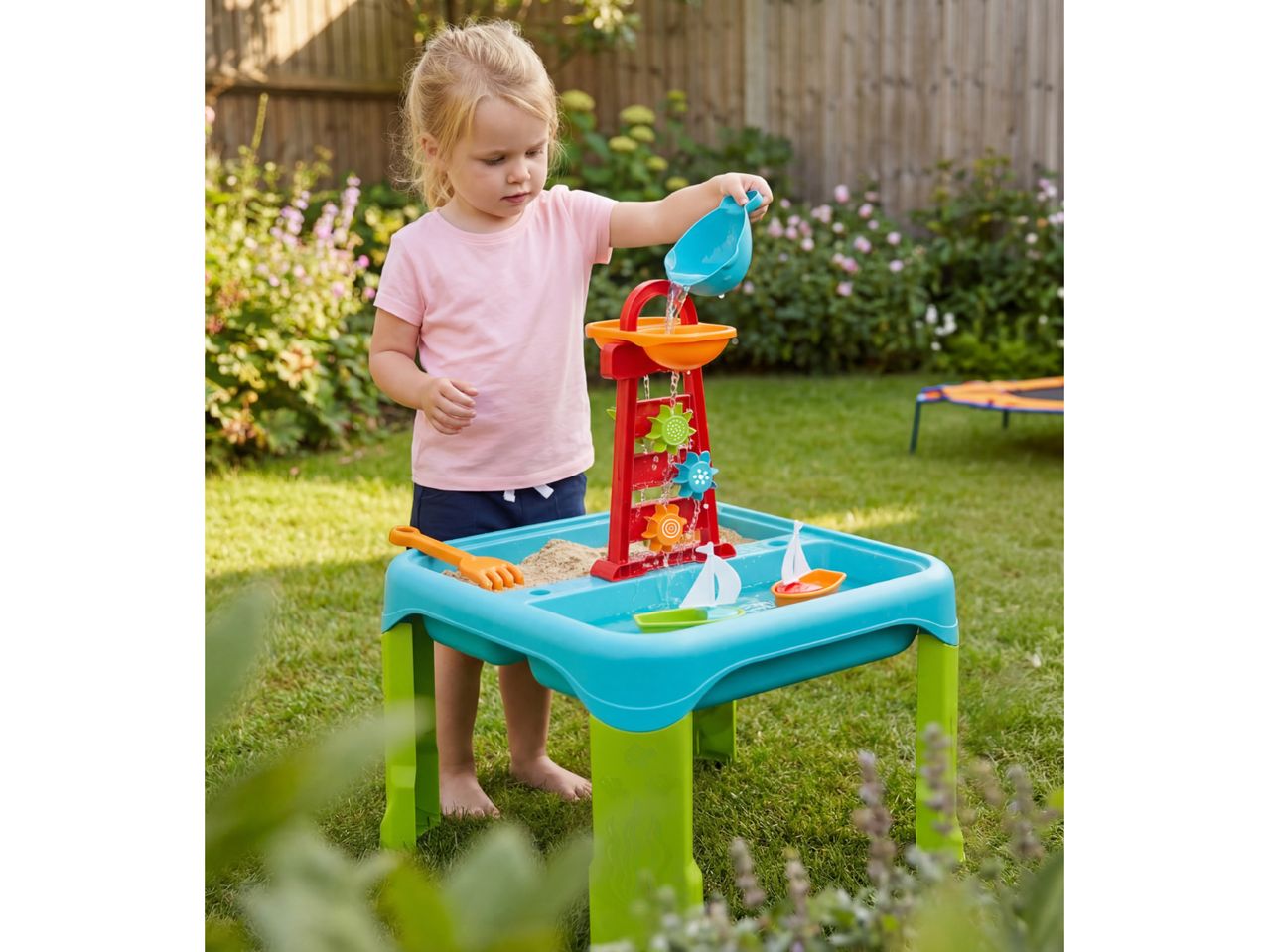 A child playing with a sand and water table in a garden.