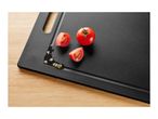 Fresh tomatoes, whole and sliced, on a black cutting board with juice and seeds.