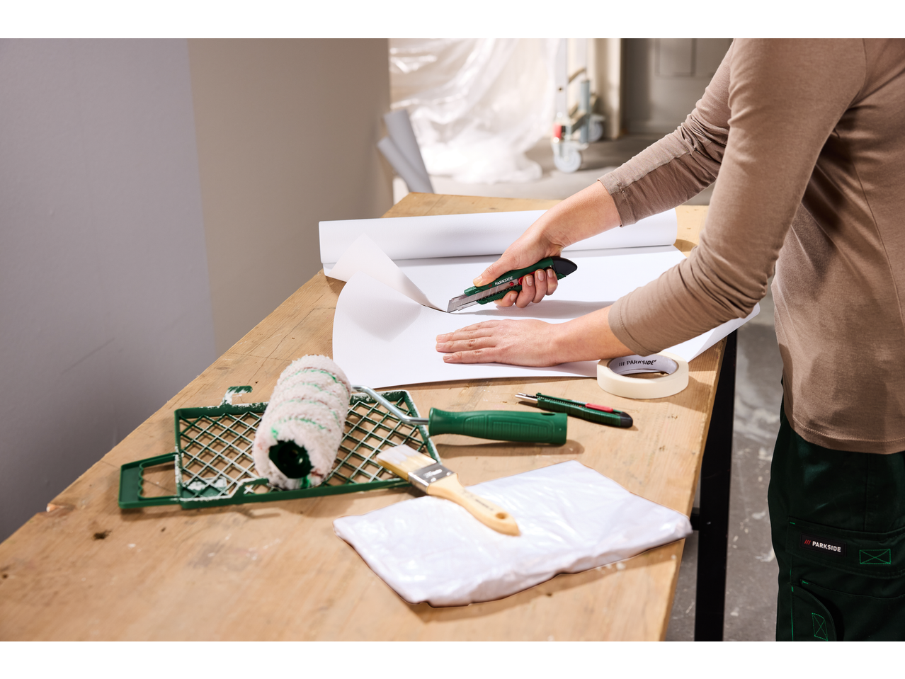 Persoană tăind hârtie cu un cutter, cu unelte de vopsit pe masă.