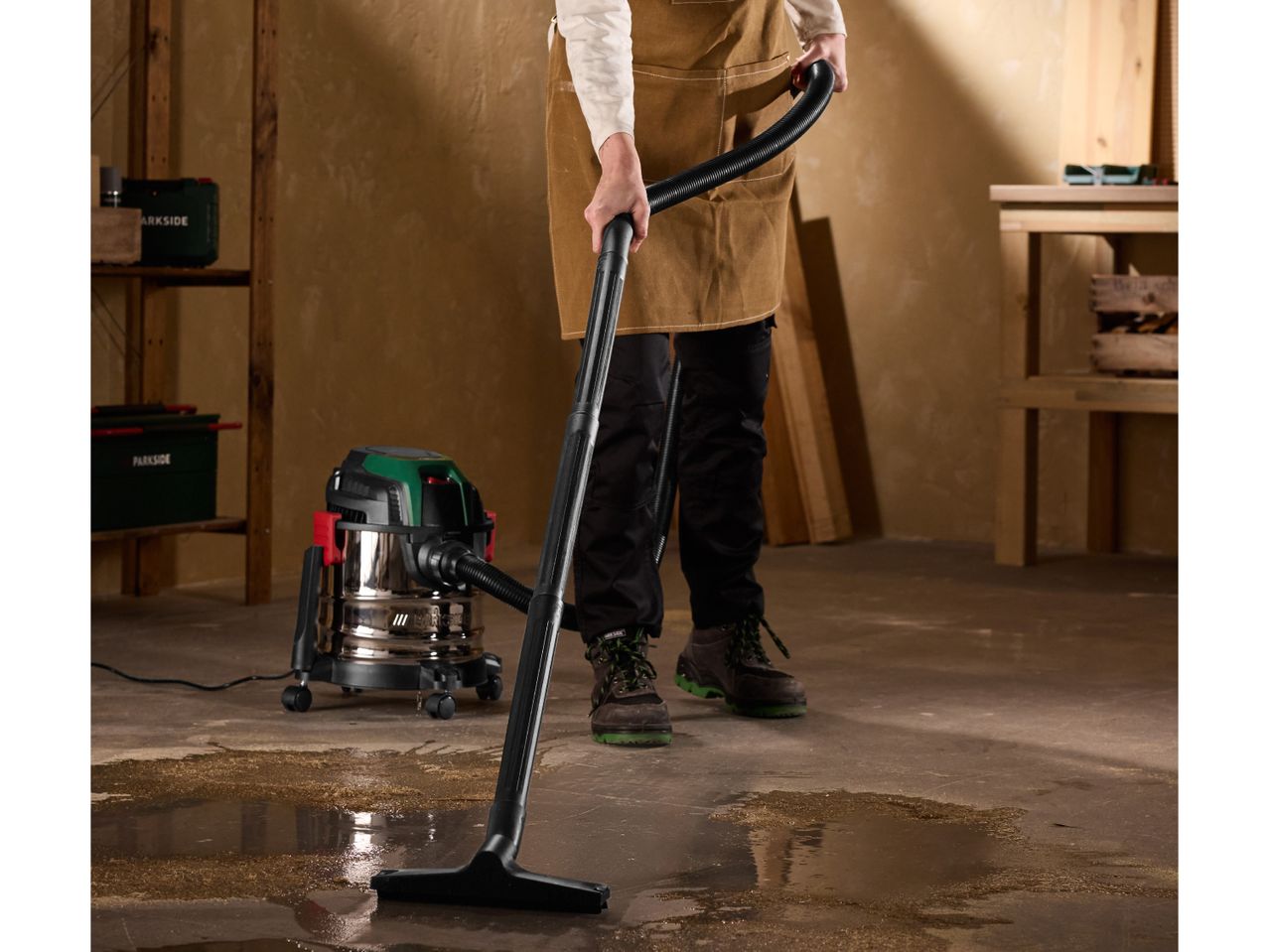 Person cleaning a workshop floor with a wet and dry vacuum cleaner, surrounded by tools.