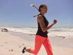 Donna che corre in pantaloncini e top neri sulla spiaggia.
