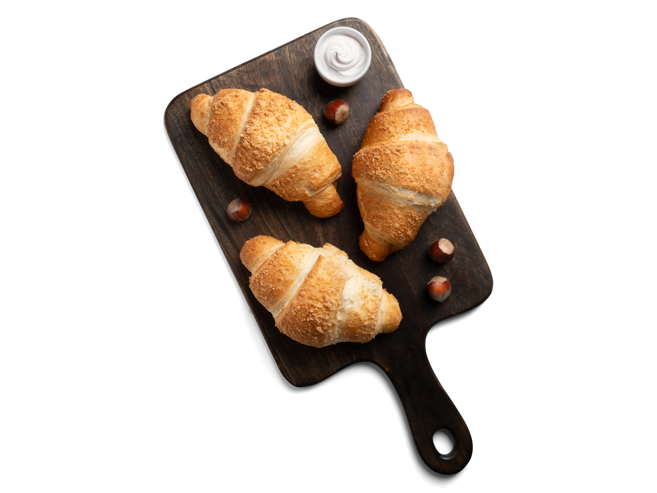 Három aranybarna croissant mogyoróval és krémmel egy sötét fa deszkán.