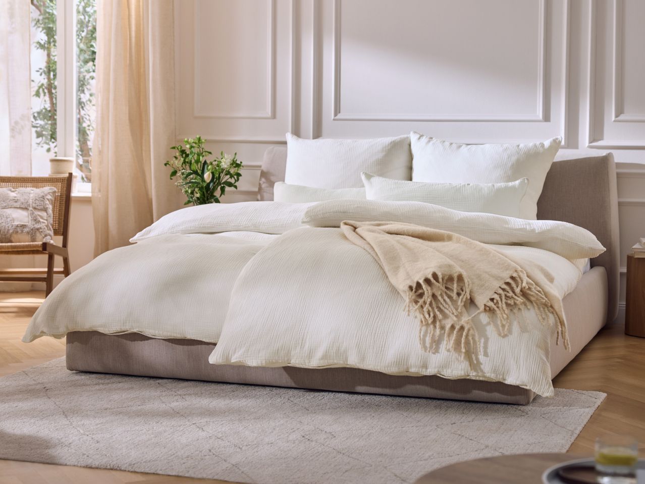 A cozy bedroom with a bed featuring white bedding, pillows, and a beige throw blanket.